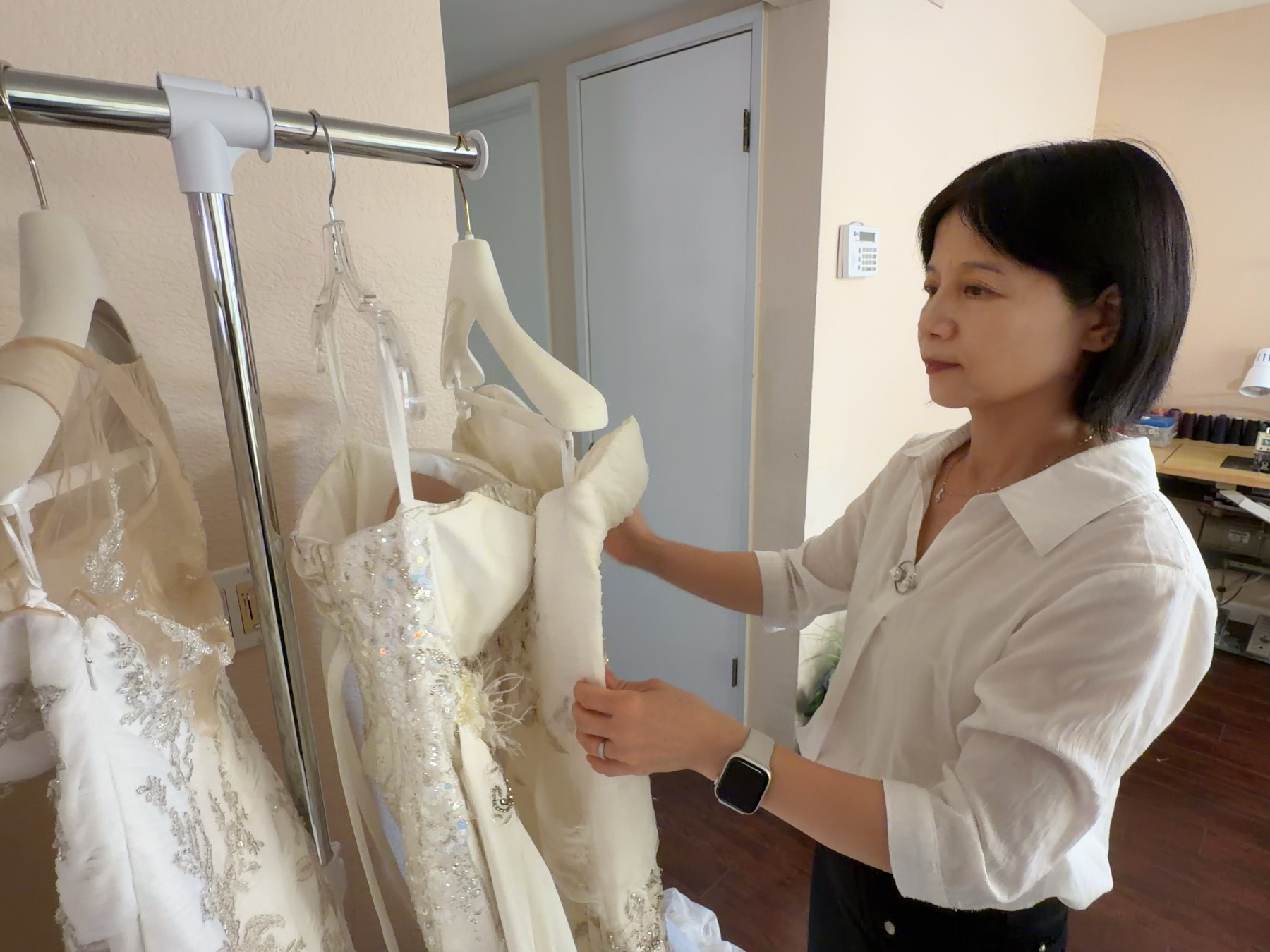 Elaine looking through wedding gowns of different silhouettes on a rack in her studio