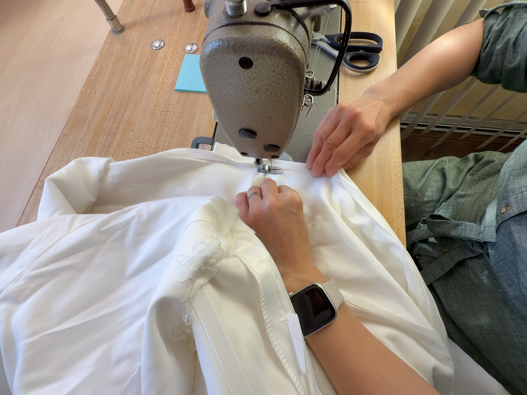 Hands guiding white bridal fabric through a sewing machine in the studio