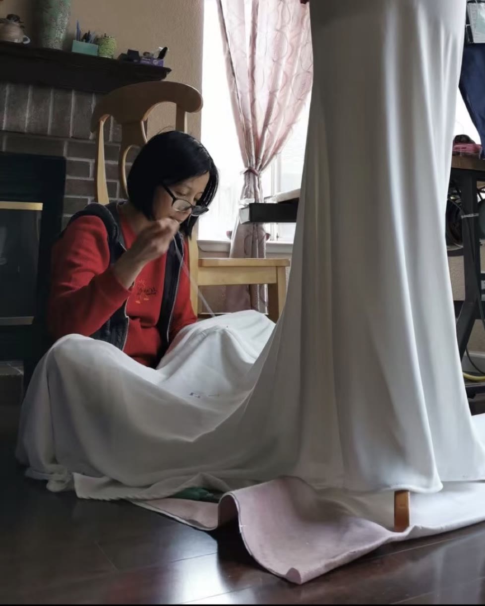 Elaine hand-finishing a wedding gown beside the dress form in her Sacramento studio